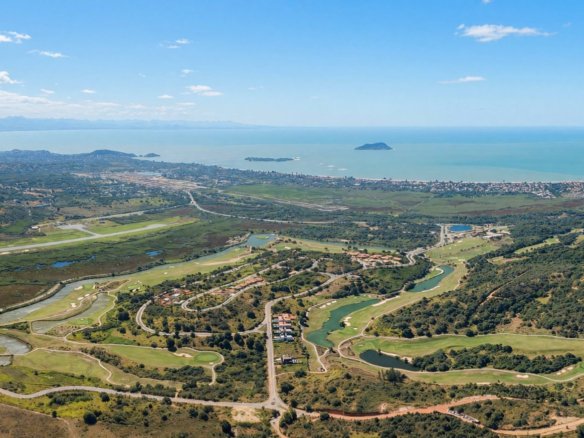 Vista aérea ilustrativa da Região Ybirá, com campo de golfe e mar ao fundo; imagem tratada por IA.