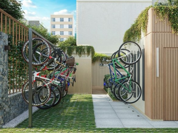 Bicicletas em suportes verticais em área externa com piso gramado e muro de pedra