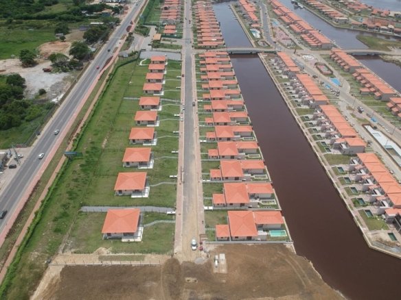 Vista aérea de um canal do Toriba entre duas fileiras de casas, com a estrada à esquerda (foto real)