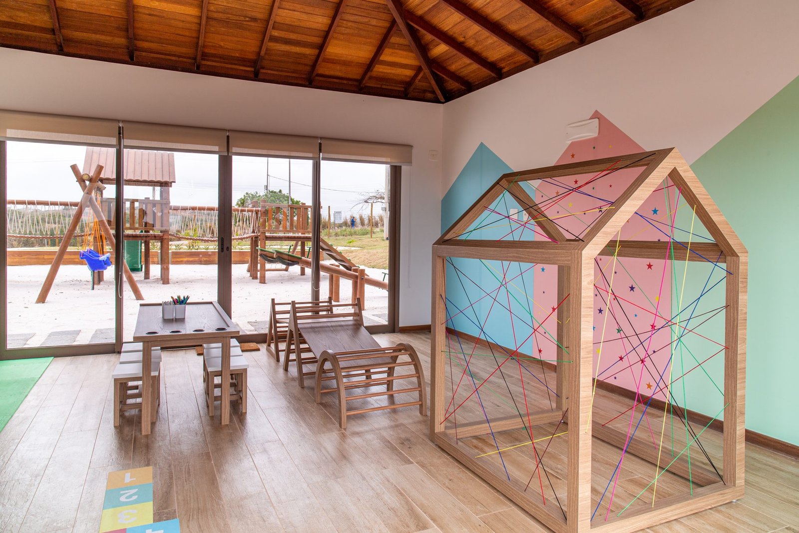 Brinquedoteca com casinha de cordas (foto real) Brinquedoteca com uma casinha de madeira e cordas coloridas, e portas de vidro para o espaço criança, no Alto Ybirá (foto real)